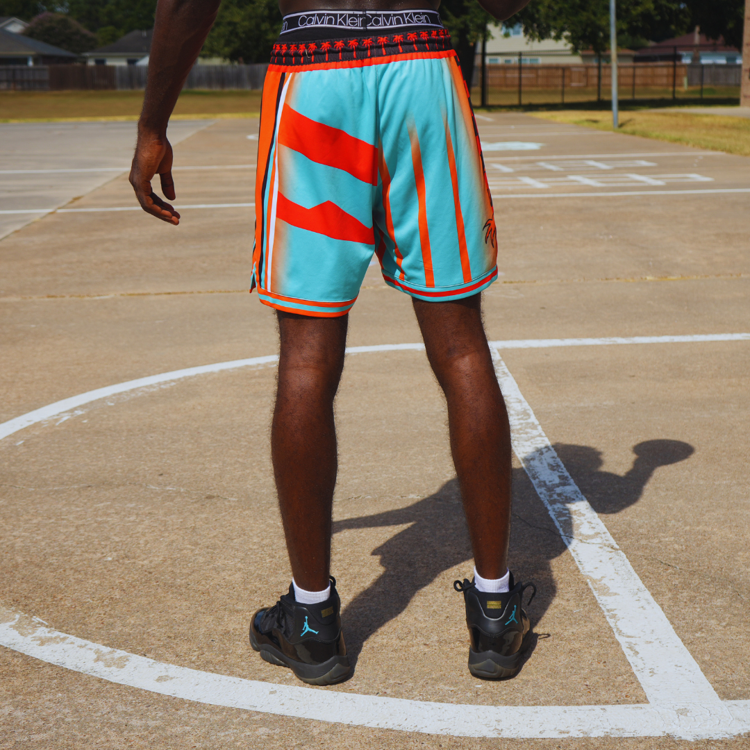 Man wearing Tropical Heat Shorts in blue and orange on outdoor basketball court with black sneakers and white socks