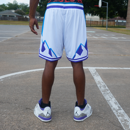 Man wearing white and blue reversible Rockies Shorts standing on an outdoor basketball court.