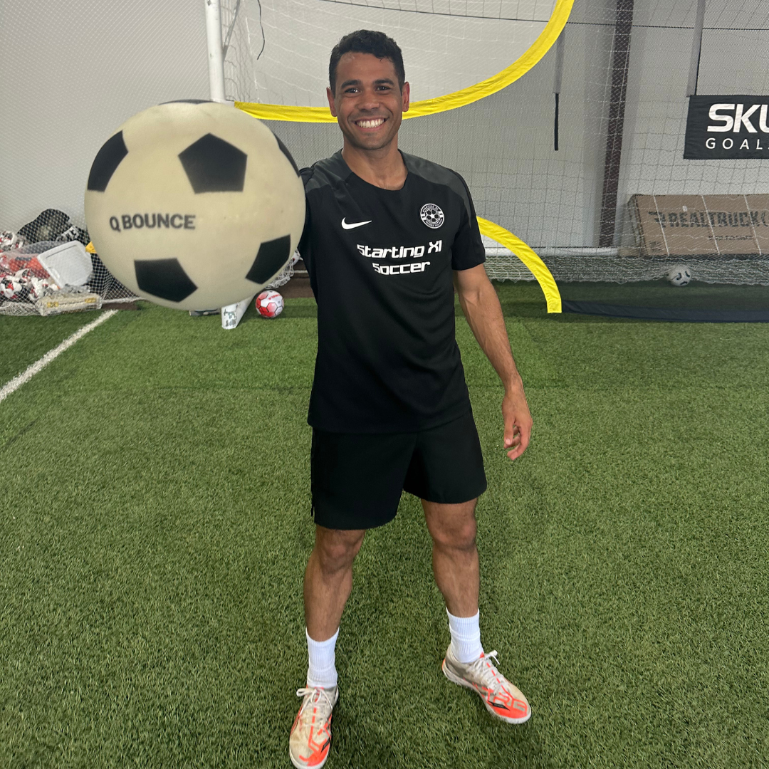 Man holding a large soccer ball on a sports field with a goal and SKLZ branding in the background.