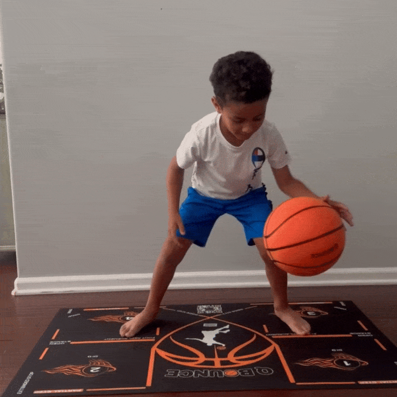 Child practicing dribbling skills on the QBounce Basketball Starter Bundle Kit dribbling mat indoors.
